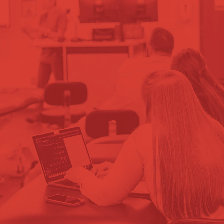 Students sitting in a classroom listening to a lecture whilst on a laptop.